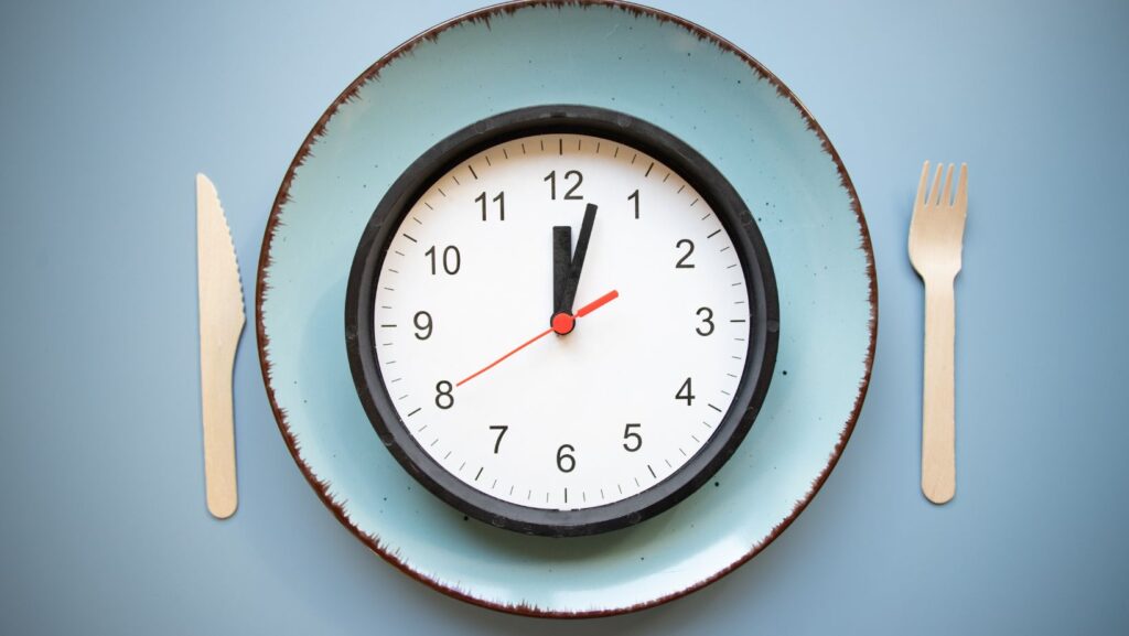 An empty plate beside a clock, representing delayed eating
